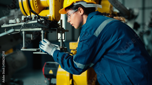 Caucasian mechatronics engineer is inspecting a lot of robotic arms in warehouse before being used in factory. A female industrial worker is using a tablet to record the results of examining machines.