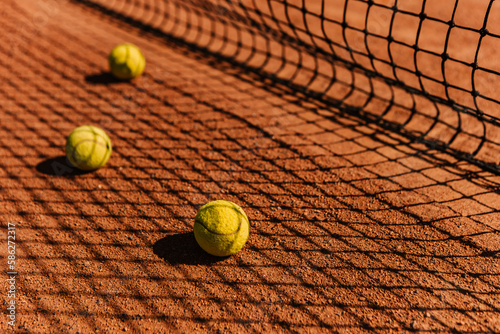 Light orange empty outdoor clay court surface dry grungy ground baseline detail for playing tennis with net shadow in sunny day, yellow green balls, gravel texture background, copy space for text 
