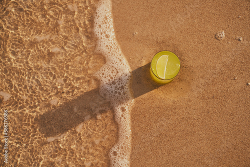Image of a refreshing lemonade on the sand by the sea. Picture of cocktail among the waves by the sea at the beach. Visual evocative of a summer vacation trip in a tropical location.