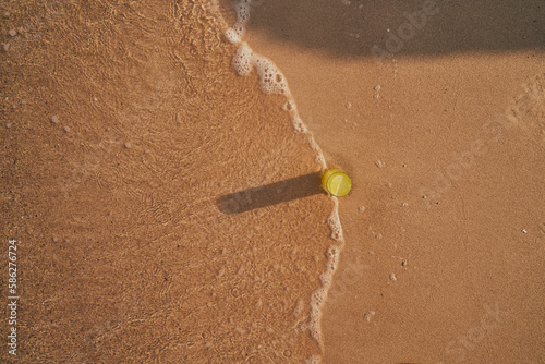 Image of a refreshing lemonade on the sand by the sea. Picture of cocktail among the waves by the sea at the beach. Visual evocative of a summer vacation trip in a tropical location.
