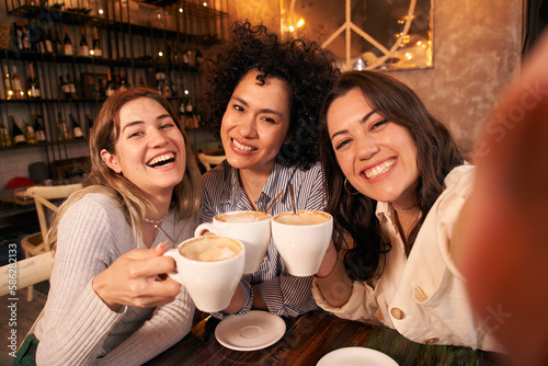 Slika na platnu Group of cheerful female friends take a selfie toasting cups of cafe in coffee shop