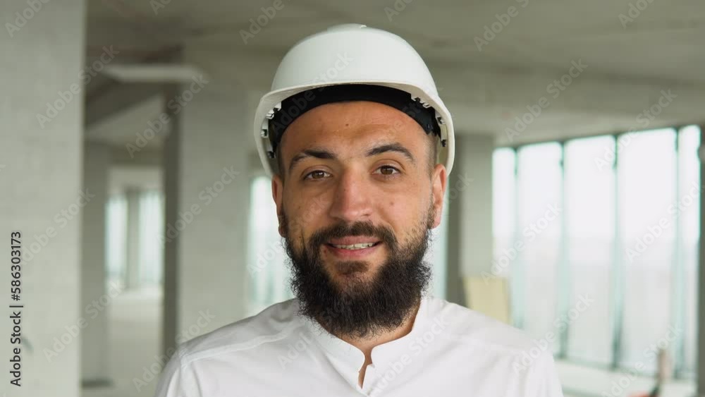 Confident Arabian Middle Eastern civil engineer wearing a safety helmet looking at the camera, standing on construction site Confident Arabian Middle Eastern civil engineer wearing a safety helmet looking at the camera, standing on construction site