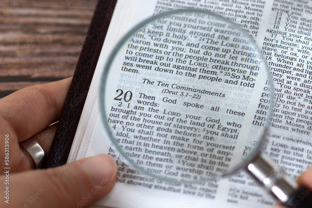 Human hand holding a magnifying glass over open holy bible book of