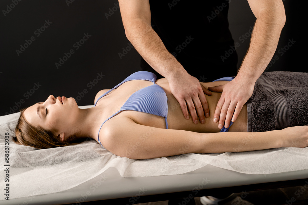 Fototapeta premium Attractive girl is relaxing on classic massage procedure in spa. Manual therapy. Masseur is doing belly massage.
