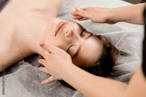 Masseur is making facial beauty treatments for attractive female model. Neck and face massage in the spa. Relaxation.