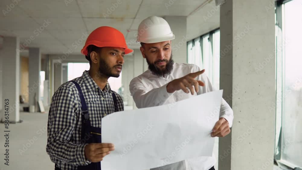 Arab architect is explaining to indian builder the plan of construction. The foreman pointing at building with seriousness Arab architect is explaining to indian builder the plan of construction. The foreman pointing at building with seriousness