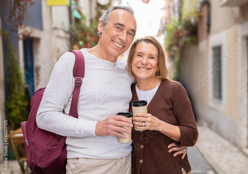Happy Mature Spouses Embracing Holding Coffee Cups Standing In Lisbon © Prostock-studio