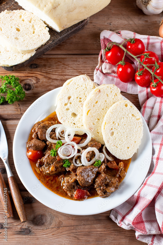 Beef goulash with bread dumplings and parsley garnish on white ceramic plate on table. Top view.