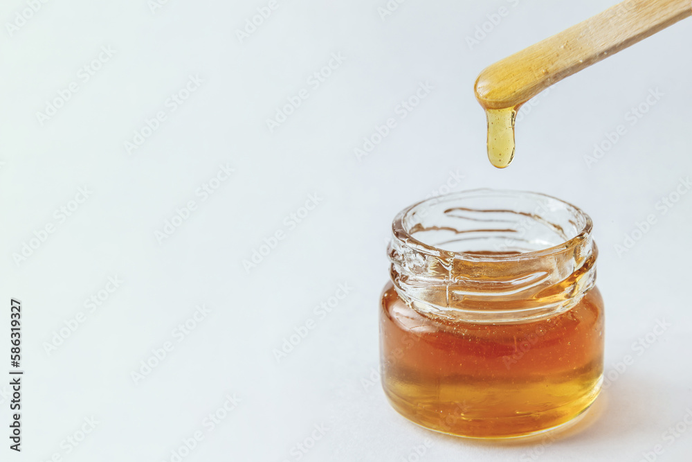 Liquid yellow sugar paste in glass jar, wooden spatula on a white background. Sugaring. Depilation. Epilation. Honey, food Liquid yellow sugar paste in glass jar, wooden spatula on a white background. Sugaring. Depilation. Epilation. Honey, food