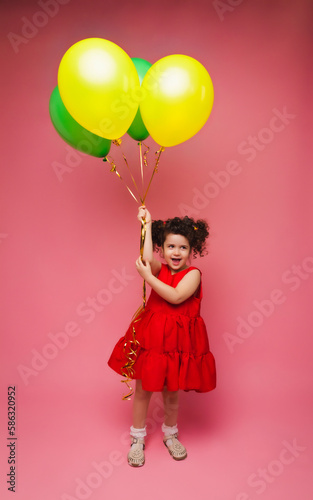 Portrait of a cheerful little girl isolated on a pink background, holding a bunch of colorful balloons, posing.