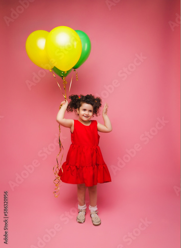 Portrait of a cheerful little girl isolated on a pink background, holding a bunch of colorful balloons, posing.