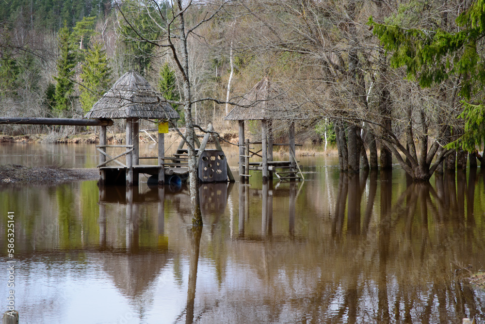 an overflowing river in a nature park where trees and children's playhouses can be seen in the water in spring an overflowing river in a nature park where trees and children's playhouses can be seen in the water in spring