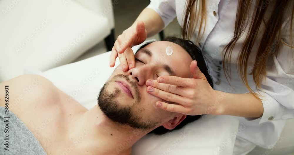 Beautician applies white skin moisturizer to handsome man's face Beautician applies white skin moisturizer to handsome man's face