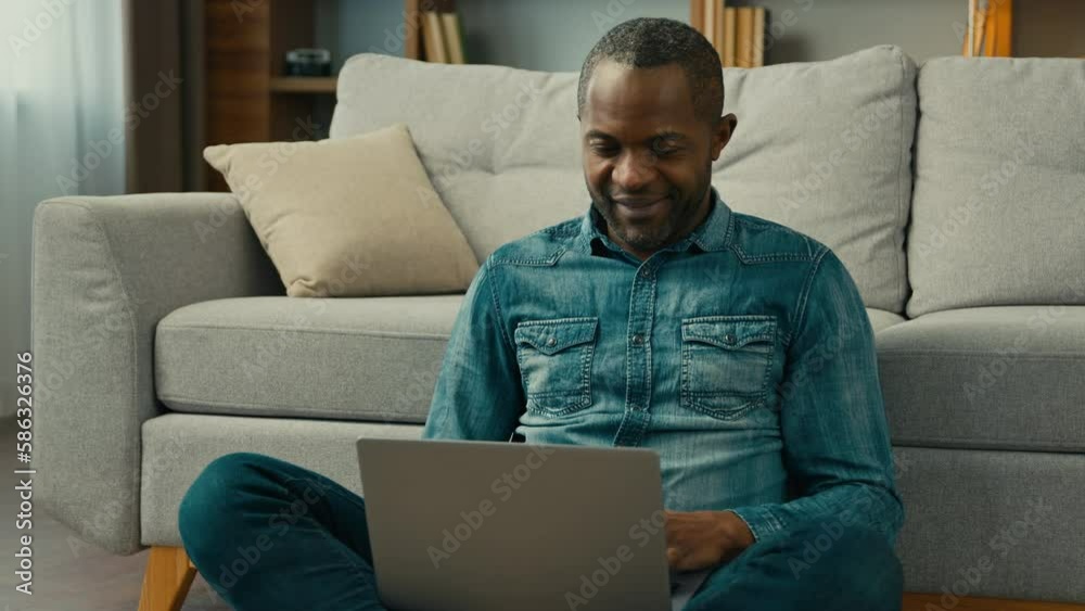 Smiling african american man typing on laptop browsing social network in cozy living room businessman freelancer working on internet at home remote work make purchase in online store using computer