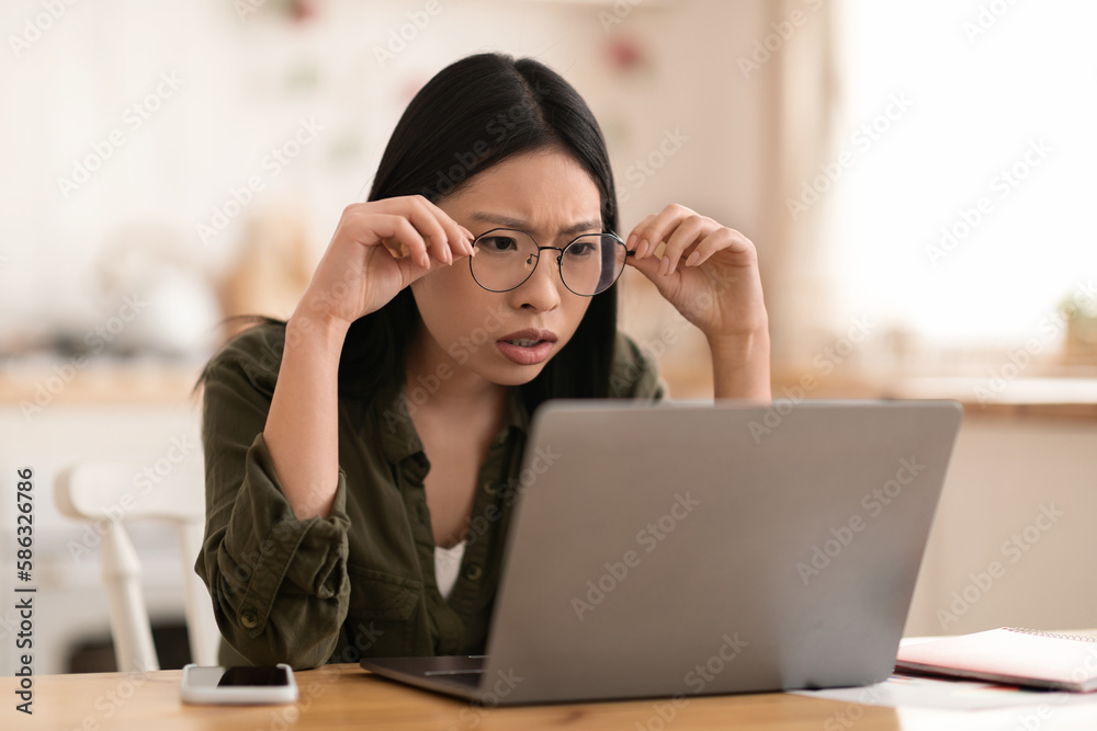 Shocked asian woman sitting at desk and looking at laptop Shocked asian woman sitting at desk and looking at laptop