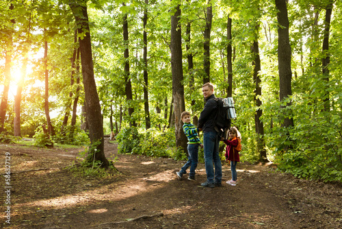 dad and two kids walk in the woods. Staycations, hyper-local travel, family outing, getaway, natural environ. copy space. Concept of friendly family. Family spends summer time together