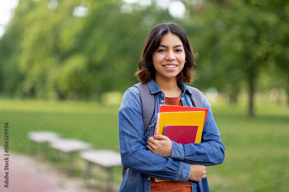 Smiling Beautiful Middle Eastern Female Student Holding Workbooks While Posing Outdoors Smiling Beautiful Middle Eastern Female Student Holding Workbooks While Posing Outdoors