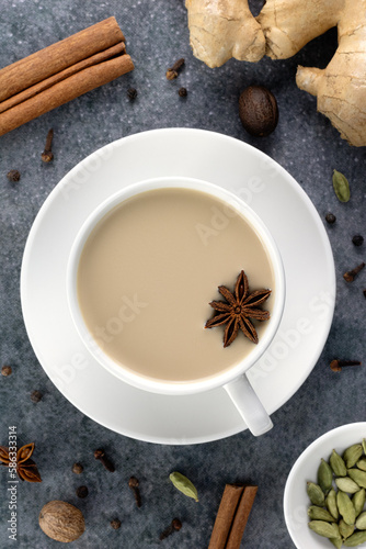 Indian masala tea in a white mug with spices - cinnamon, star anise, ginger, cloves, cardamom on a gray background.