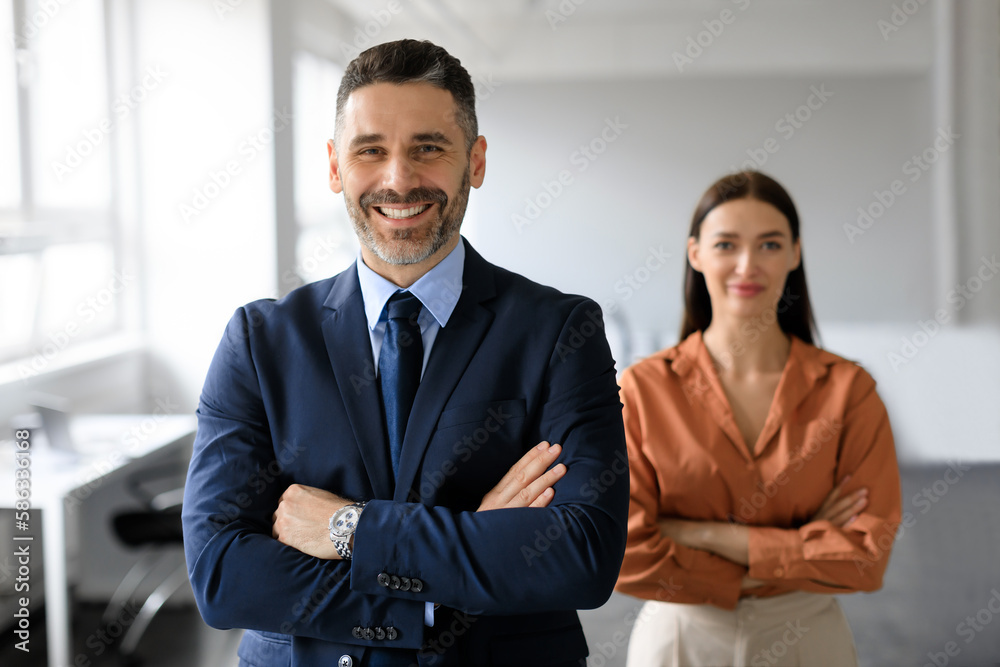 Portrait of two business leaders partners posing with folded arms and smiling at camera, working together in office Portrait of two business leaders partners posing with folded arms and smiling at camera, working together in office