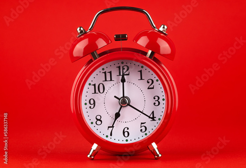 Red alarm clock on a red background. It's 7 o'clock on the clock. Morning. 