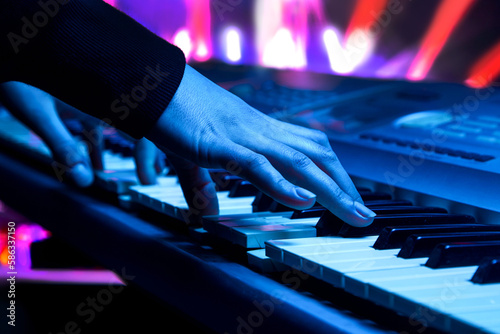close-up of the hands of a musician playing a synthesizer against the backdrop of concert spotlights