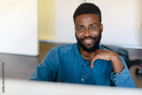 Portrait of happy black businessman sitting at desk with computer  working in office and smiling at camera  copy space