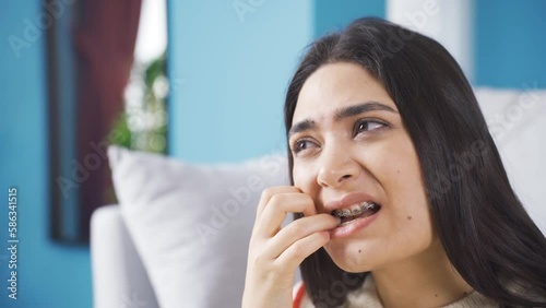 Young woman with gum pain suffers from pain and ache.
Young woman with braces at home has aching teeth, weak gums, unhappy with pain and restless.
