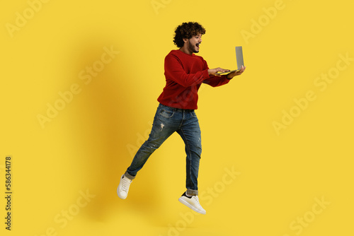 Excited hindu guy using laptop and jumping up
