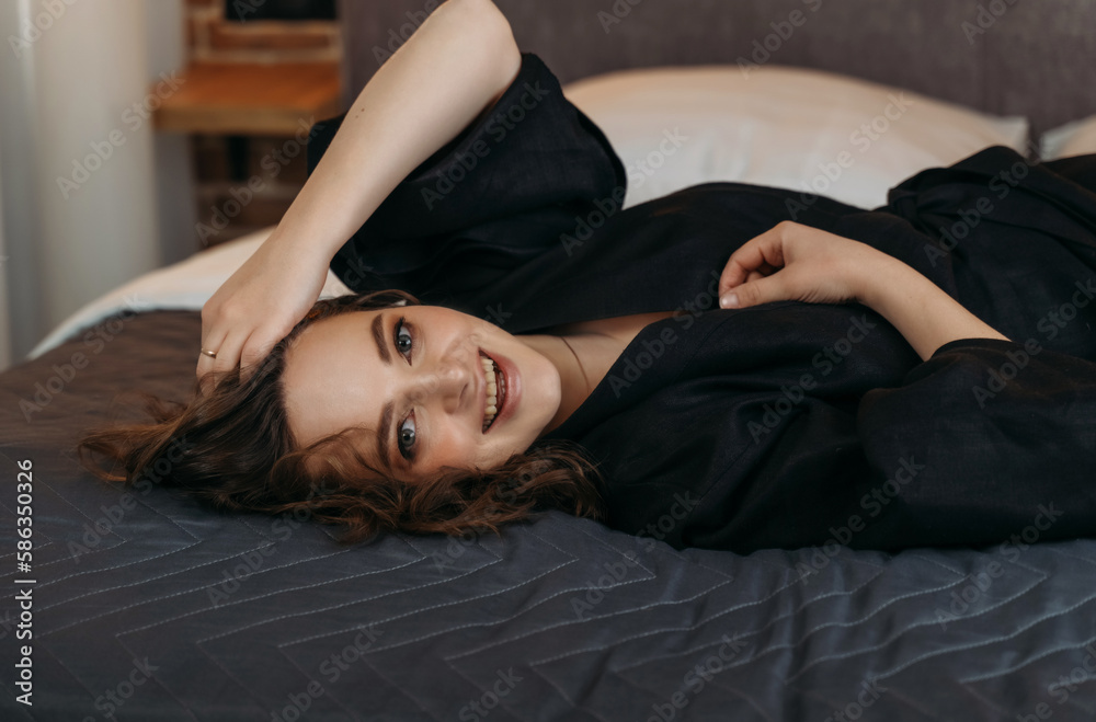 Beautiful woman in bed, stretched out in her pajamas, looks back at the camera, smiles Beautiful woman in bed, stretched out in her pajamas, looks back at the camera, smiles