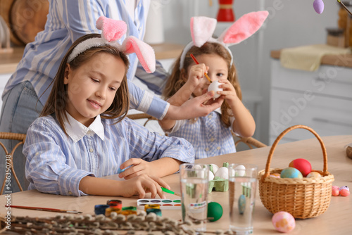 Little girls painting Easter eggs with mother at table in kitchen