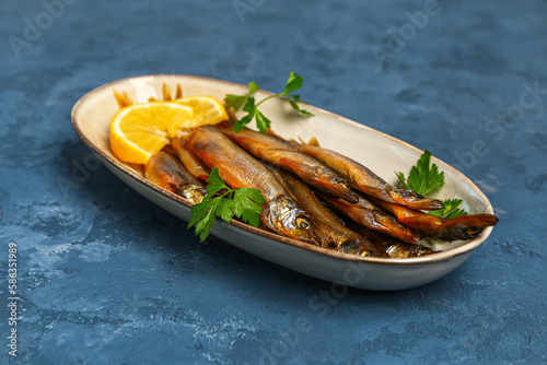 Plate with delicious smoked capelin on blue grunge background photo