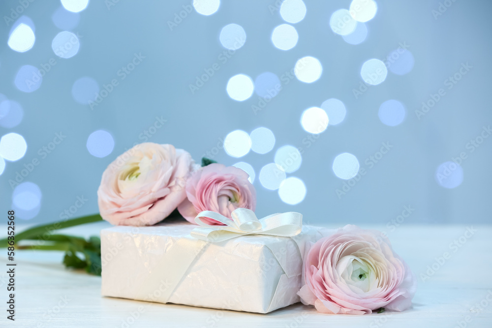 Gift and beautiful ranunculus flowers for Mother's Day celebration on table against blurred lights Gift and beautiful ranunculus flowers for Mother's Day celebration on table against blurred lights