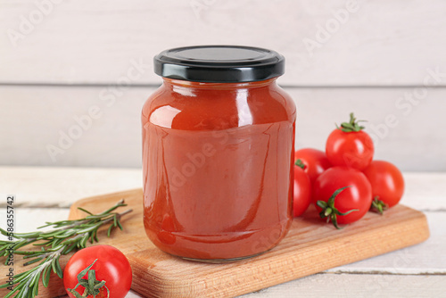 Board with jar of tasty tomato paste on white wooden background