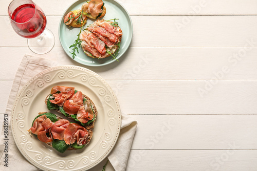 Plates of tasty bruschettas with ham on white wooden background