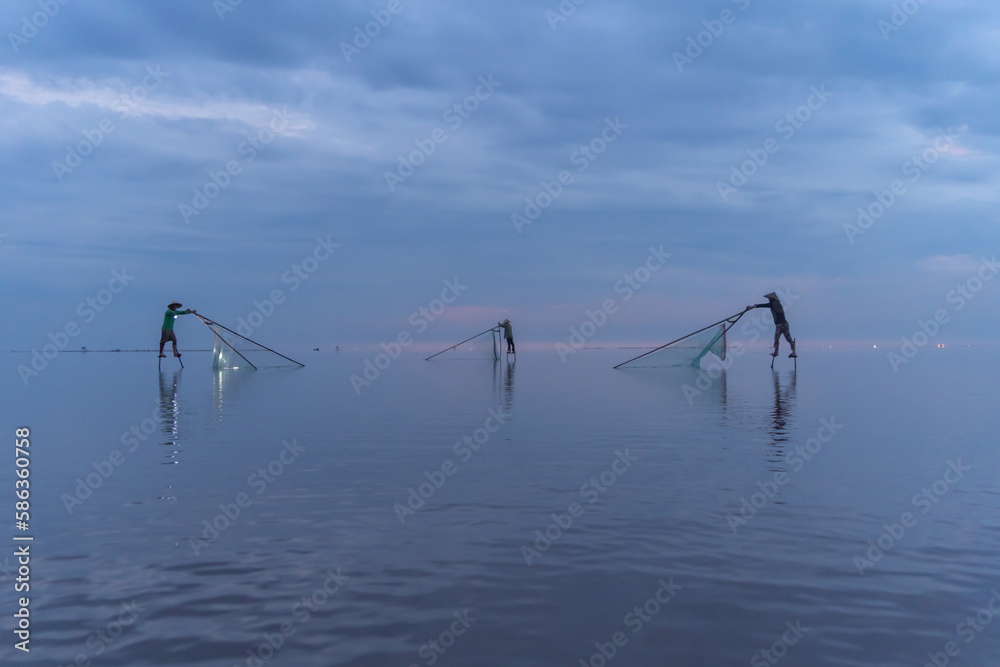Fototapeta premium Silhouette of Vietnamese fisherman holding a net for catching freshwater fish in nature lake or river with reflection in morning time in Asia in Vietnam. People.
