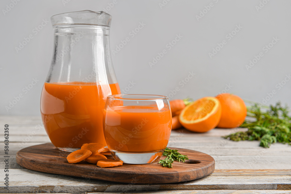 Glass, jug of fresh carrot juice and oranges on grey wooden table