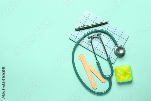 Stethoscope, notebook and pills on turquoise background