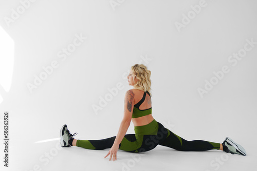 an attractive blonde in a tracksuit sits on the twine on a white background. 