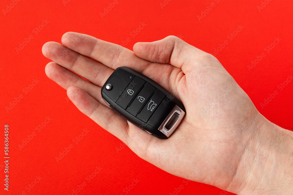 A man's hand holds the car key isolated on a red background close up. A man's hand holds the car key isolated on a red background close up.