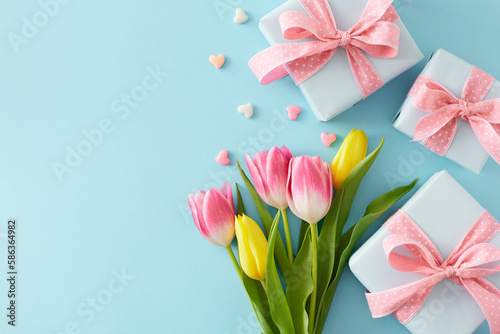 Fototapeta Naklejka Na Ścianę i Meble -  Flat lay composition of gift boxes with bows bouquet of flowers colorful tulips hearts baubles on isolated pastel blue background with empty space. Happy Mother's Day concept