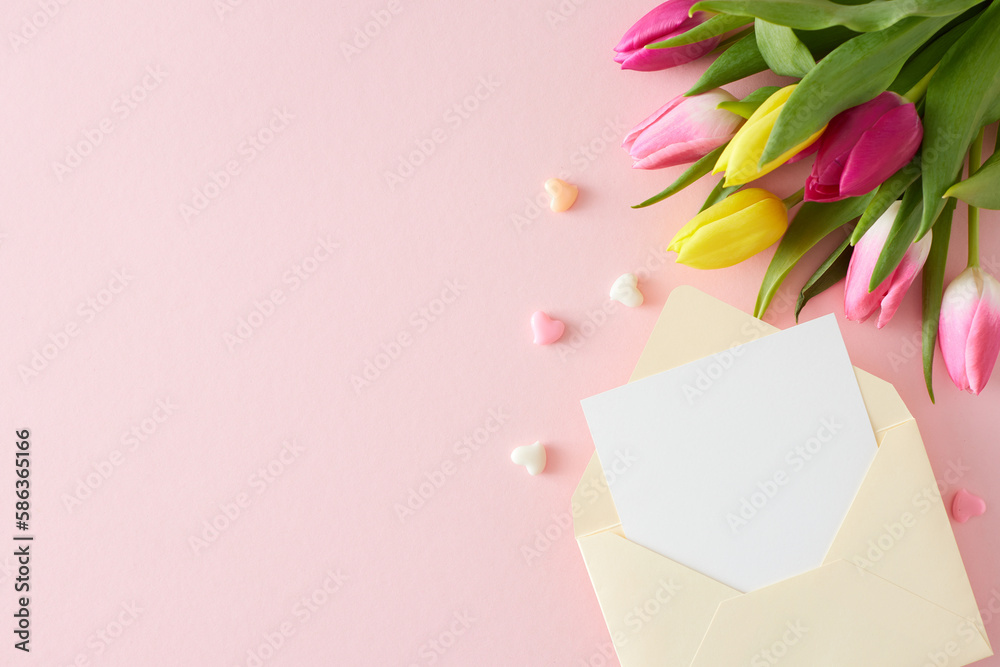 Obraz premium Top view photo of open envelope with white card bouquet of flowers yellow pink tulips and colorful hearts on isolated pastel pink background with empty space. Happy Mother's Day idea