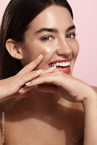 Beautiful young woman with clean perfect skin. Portrait of beauty model with natural nude make up and touching her face. Spa  skincare and wellness. Close up  pink background  copyspace