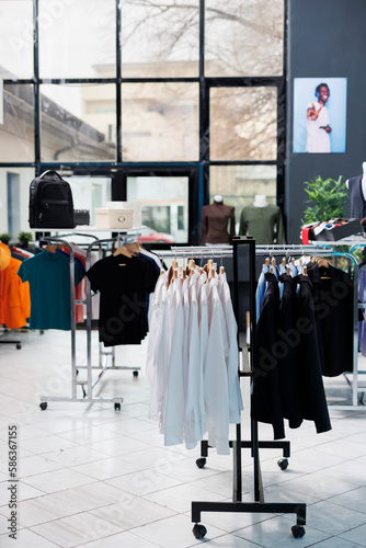 Interior of fashionable boutique with clothes on hangers, stylish brand design and formal wear in modern showroom. Empty clothing store in shopping center with trendy merchandise, commercial activity.