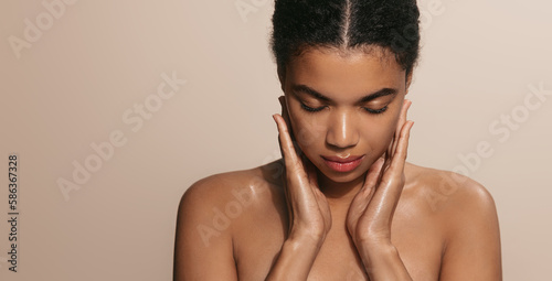 Portrait of african american girl washing her face, using cleansing moisturizing gel, skincare cosmetics, standing over brown background