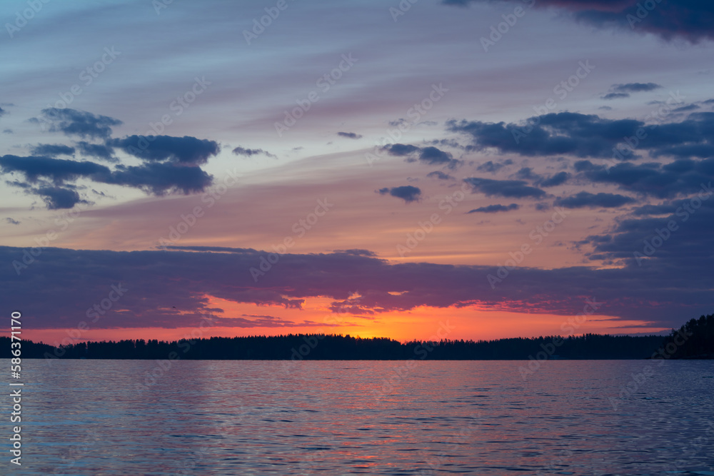 Purple colored clouds over a forest and a lake just after sunset