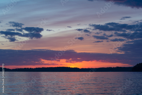 Purple colored clouds over a forest and a lake just after sunset