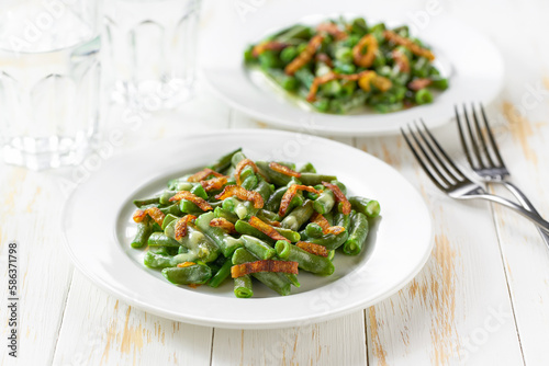 two plates with traditional green bean casserole sprinkled with crispy fried onions  on a white wooden table.