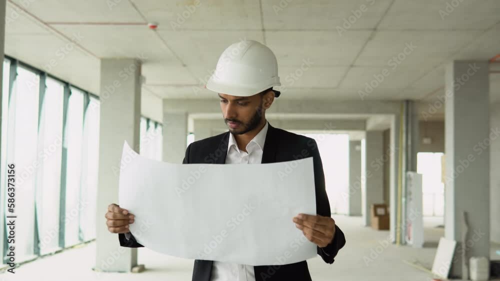 Serious attractive indian industrial engineer in hard hat with project drawings at construction of a skyscraper. Professional and industry, builder architect job, worker checking work at plant indoor Serious attractive indian industrial engineer in hard hat with project drawings at construction of a skyscraper. Professional and industry, builder architect job, worker checking work at plant indoor