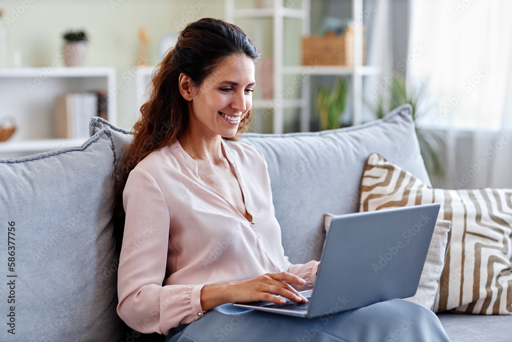 Portrait of smiling young woman using laptop while sitting on sofa at home and using internet or working online Portrait of smiling young woman using laptop while sitting on sofa at home and using internet or working online