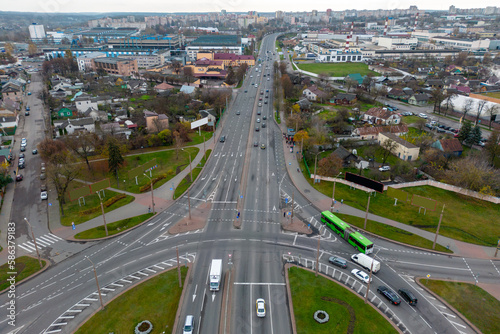 Top view of a major road junction in the city during the day. A large busy roundabout. Urban traffic and infrastructure. Green spaces inside the intersection.
